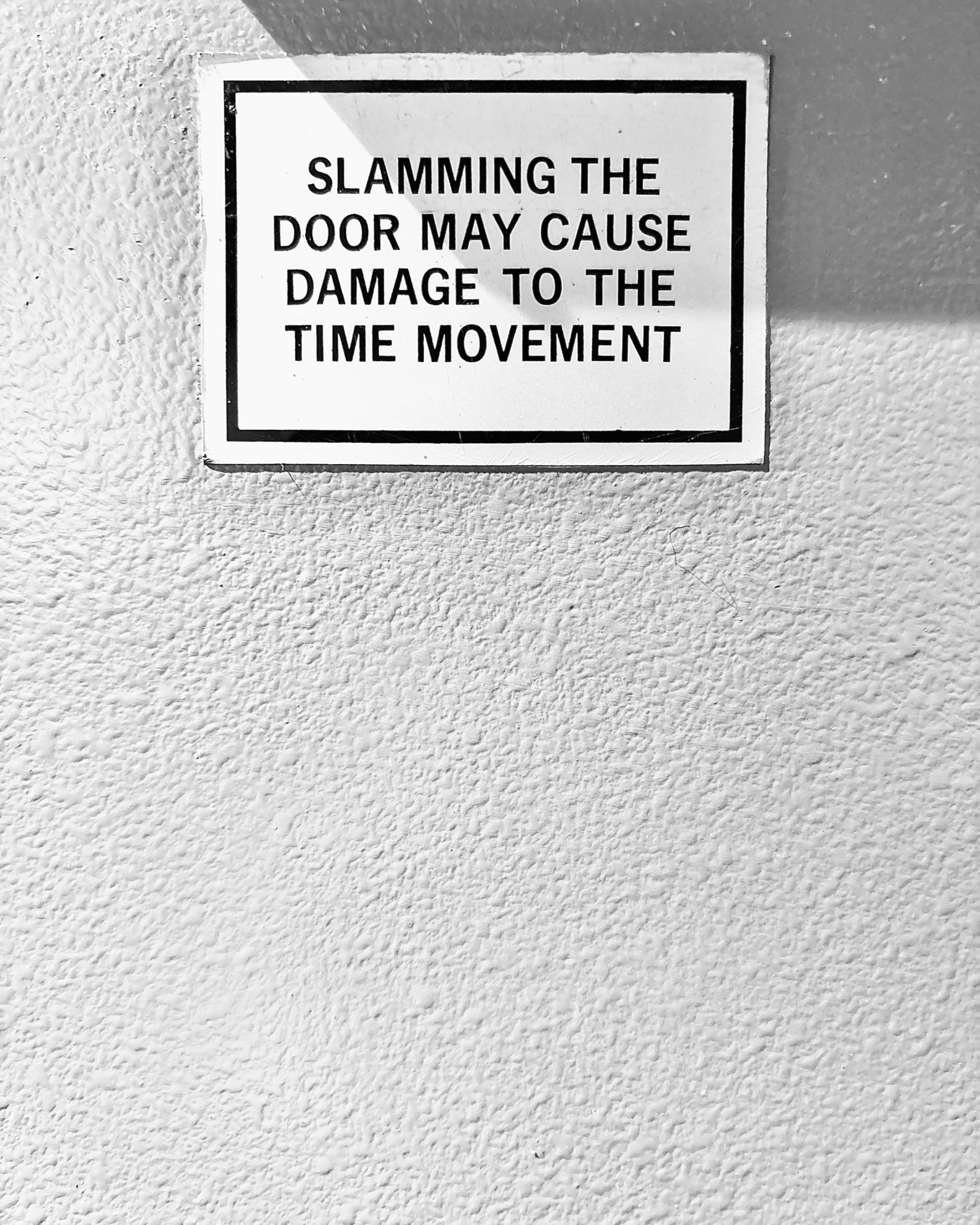 A monochrome photo of a sign stating "Slamming the door may cause damage to the time movement"